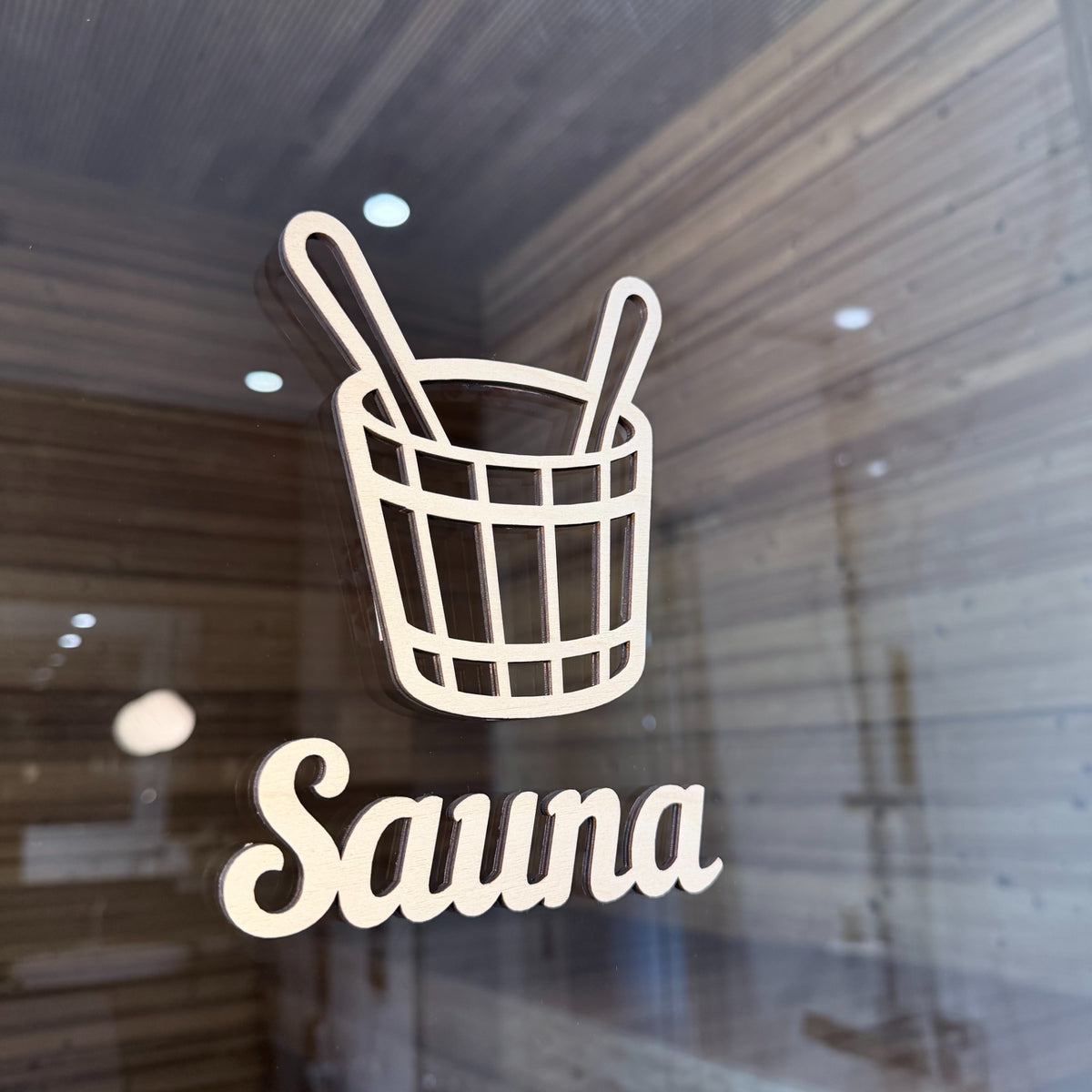 Puinen saunakiulu-kyltti saunan lasiovessa